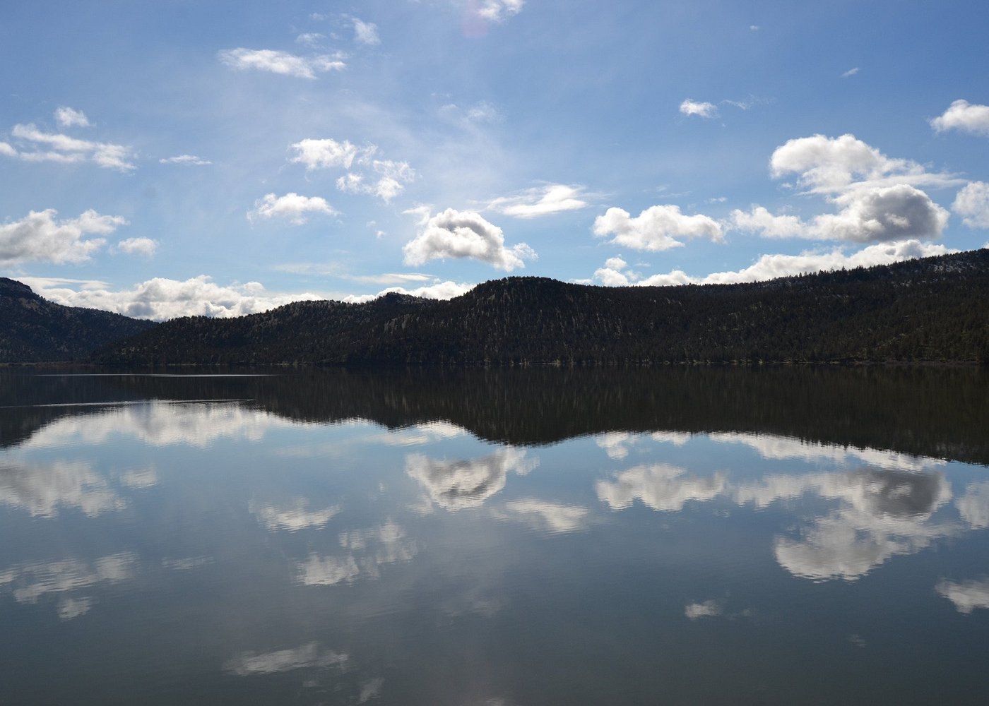 Mirror-calm Ochoco Reservoir reflecting clouds and forested ridges, across the highway from Lakeshore RV Park